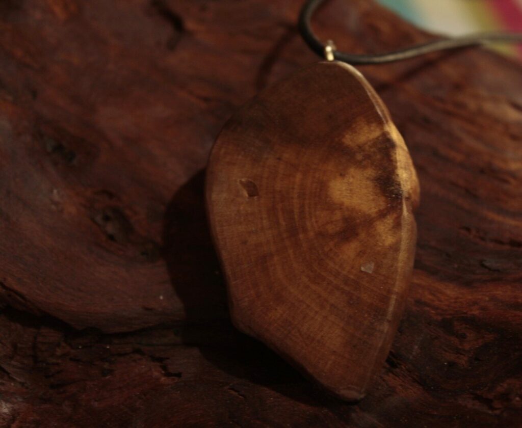 Pendentif plat en bois clair veiné, posé sur une écorce