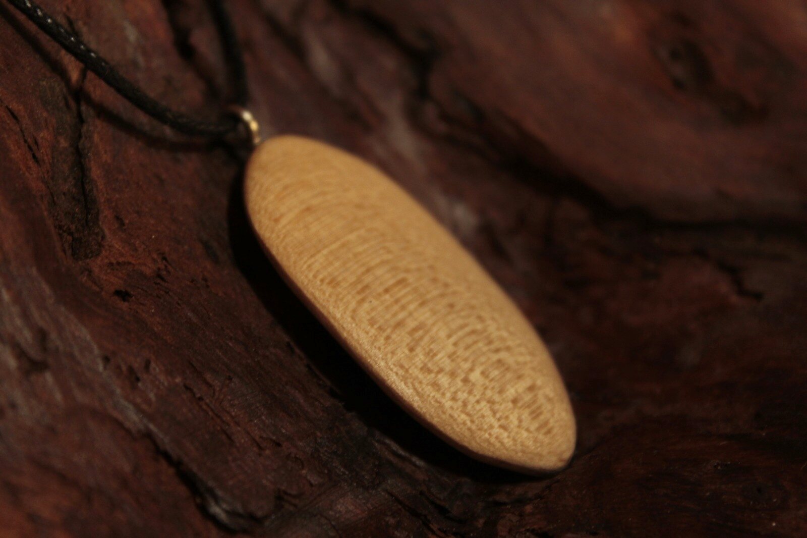 Pendentif ovale en bois clair au grain moucheté, sur une écorce sombre